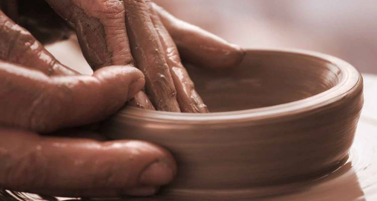 Primer plano de manos cubiertas de arcilla dando forma a un cuenco de cerámica en un torno.