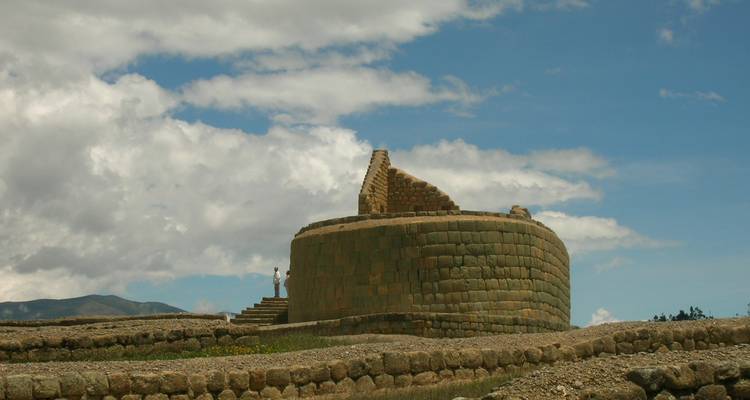 Ruinas del templo solar de piedra de Ingapirca que se alzan contra un cielo brillante y colinas ondulantes.