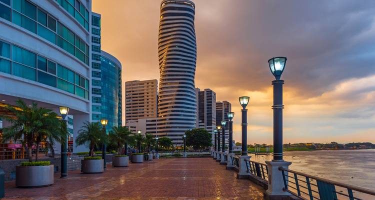 Vista del atardecer a lo largo del malecón de Guayaquil con modernos edificios de gran altura y lámparas reflejándose en los ladrillos húmedos.