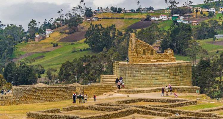 Vista amplia de las ruinas de piedra de Ingapirca ubicadas en colinas verdes ondulantes con pequeños grupos de visitantes explorando el sitio arqueológico