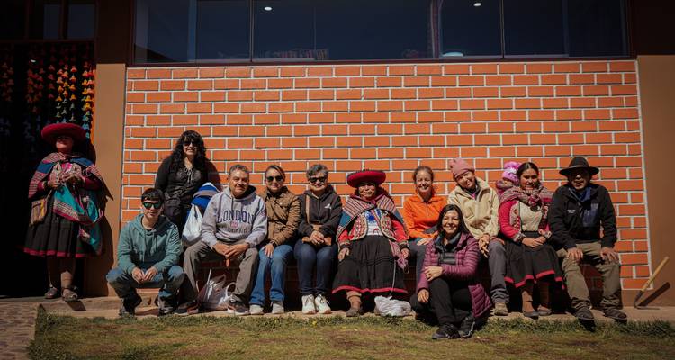 Anfitriones locales y viajeros se sientan juntos frente a una pared de ladrillo rojo, sonriendo para una foto grupal.
