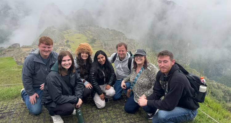 Los viajeros se agachan juntos en la cima de un mirador brumoso con vista a las ruinas de Machu Picchu.