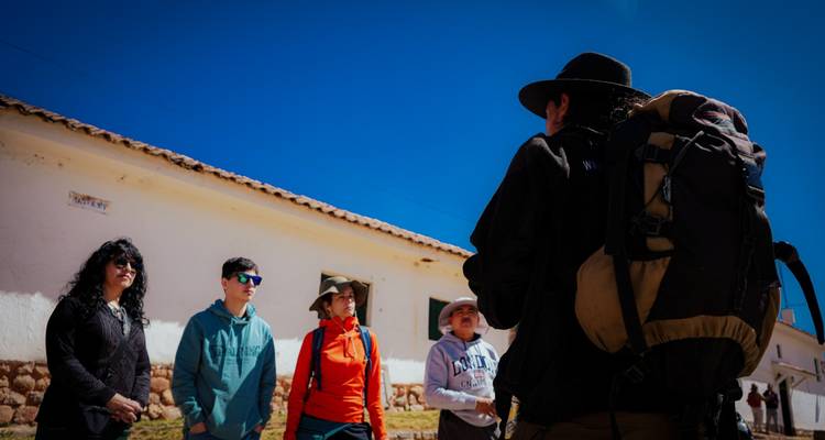 El guía habla a los viajeros fuera de un edificio de adobe bajo el brillante cielo andino.