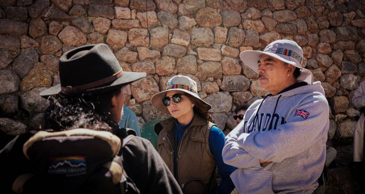Los turistas escuchan atentamente a un guía local contra una pared de piedra inca.