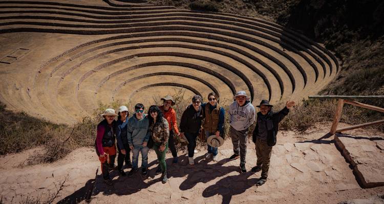 Un grupo de viajeros sonriendo para una foto en un mirador sobre las terrazas agrícolas concéntricas de Moray en el Valle Sagrado de Perú.