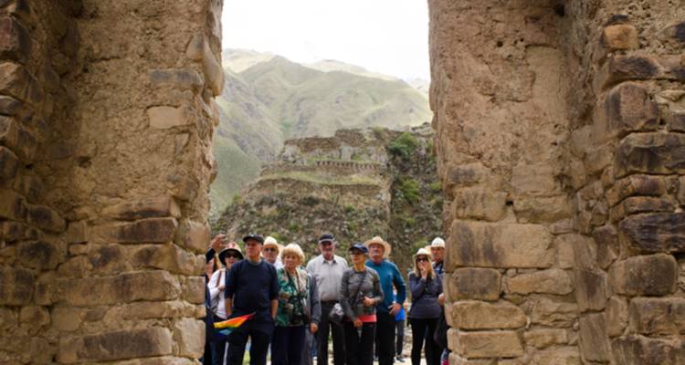 Grupo de turistas de pie entre enormes postes de piedra de una ruina inca con paisaje montañoso al fondo.