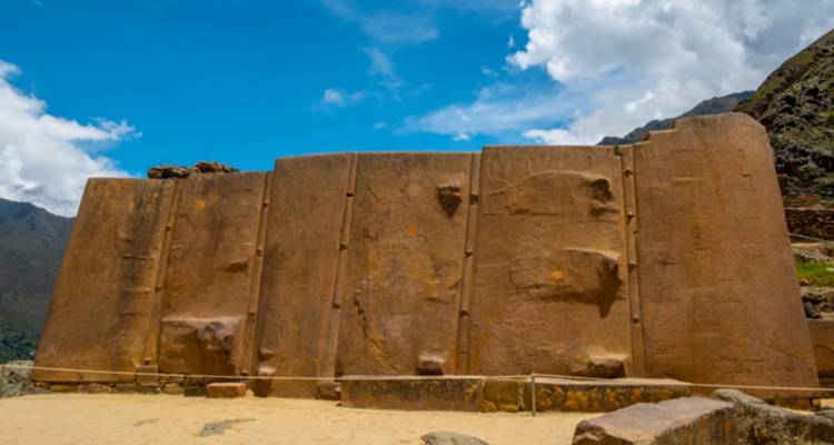 Vista frontal de primer plano de los grandes monolitos tallados de una pared inca contra un cielo azul vívido.