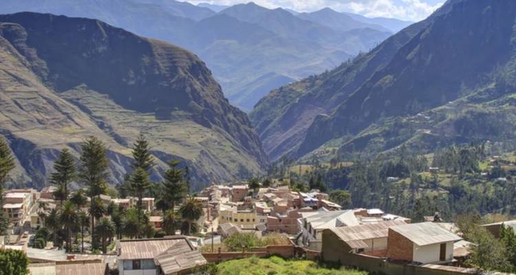 A small Andean village nestles in a steep valley surrounded by towering green mountains.