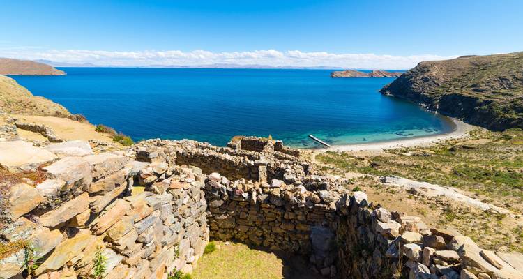 Bright view over stone Inca ruins overlooking the deep blue waters and rugged coastline of Lake Titicaca.