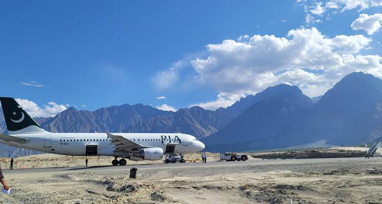 PIA passagiersvliegtuig geparkeerd op een afgelegen landingsbaan omlijst door ruige hoge bergen en verspreide wolken.