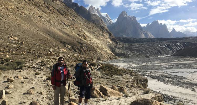 Twee trekkers met rugzakken staan op een rotsachtig pad met iconische granieten torenspitsen die erachter oprijzen.