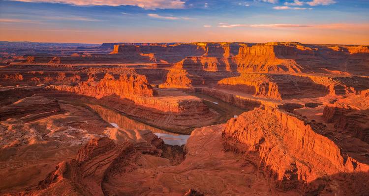Un vasto cañón de roca roja con un río serpenteante resplandece bajo la luz del final del día en Dead Horse Point.