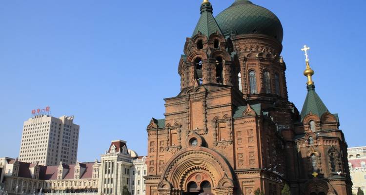 A clear view of Saint Sophia Cathedral, a red-brick Russian Orthodox church with green domes under a blue sky.