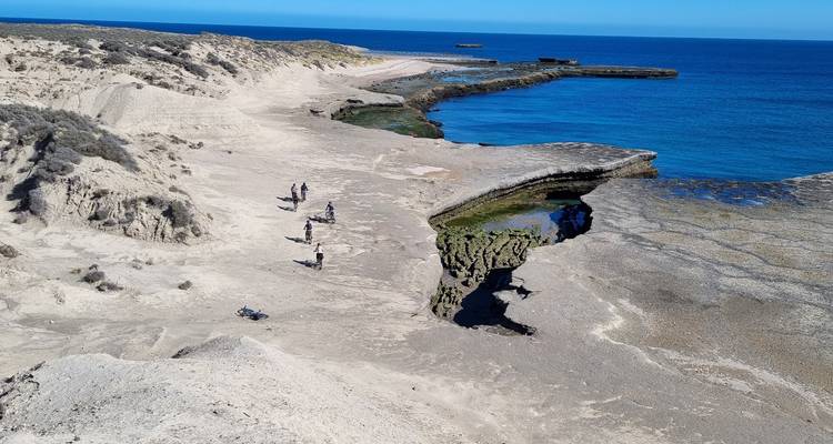 Paysage côtier aride avec des cyclistes roulant le long de falaises pâles au bord des eaux turquoise de la mer.