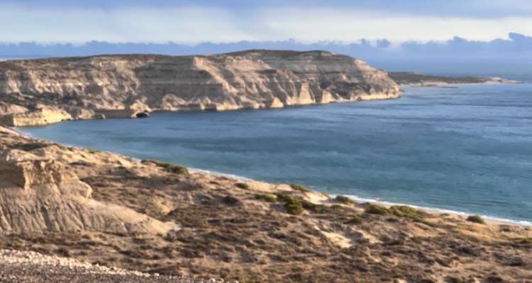 Vue légèrement douce du littoral avec des falaises calcaires bordant une baie bleue calme.