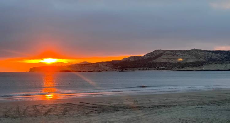 Coucher de soleil orange ardent se reflétant sur les eaux calmes de la baie avec des collines stratifiées au loin.