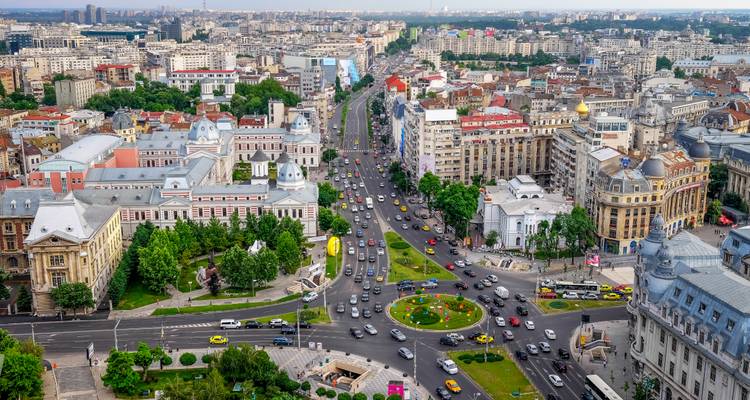 Vista aérea amplia de los bulliciosos bulevares de Bucarest, bloques de ciudad densamente poblados y una rotonda llena de tráfico en un día despejado.