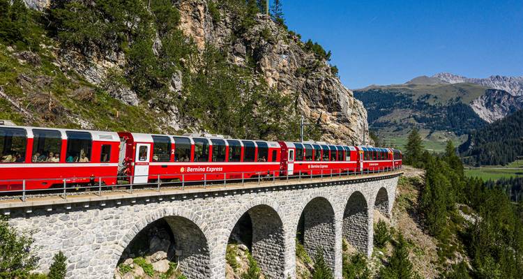 Roter Bernina Express-Zug überquert ein hohes steinernes Viadukt in den Schweizer Alpen.