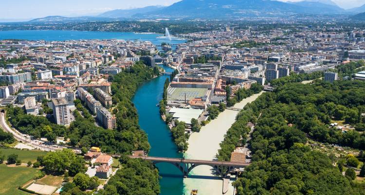 Vue aérienne de Genève montrant le Jet d'Eau, la confluence bleue et verte des rivières, et le paysage urbain environnant avec les Alpes au-delà