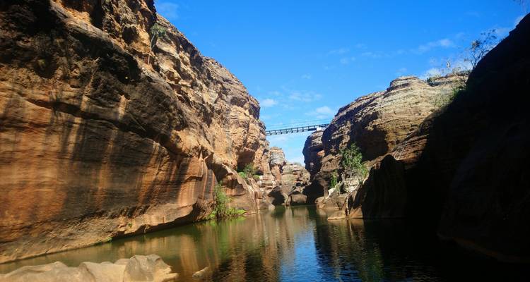 Gorge étroite remplie d'eau stagnante, parois de grès à pic et un petit pont au-dessus.