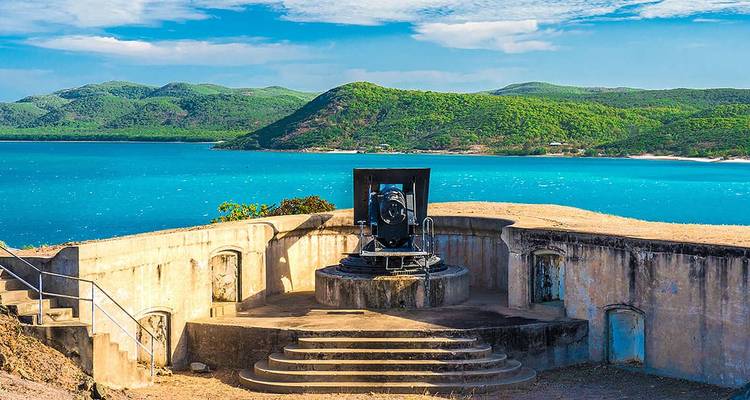 Emplacement de canon côtier historique surplombant des mers d'un turquoise éclatant et des collines verdoyantes ondulantes par une belle journée ensoleillée.