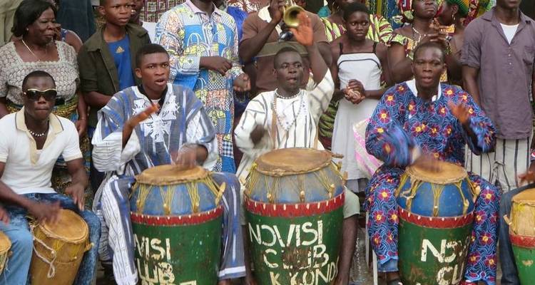Des percussionnistes africains énergiques jouant sur des tambours en bois peints devant une foule.