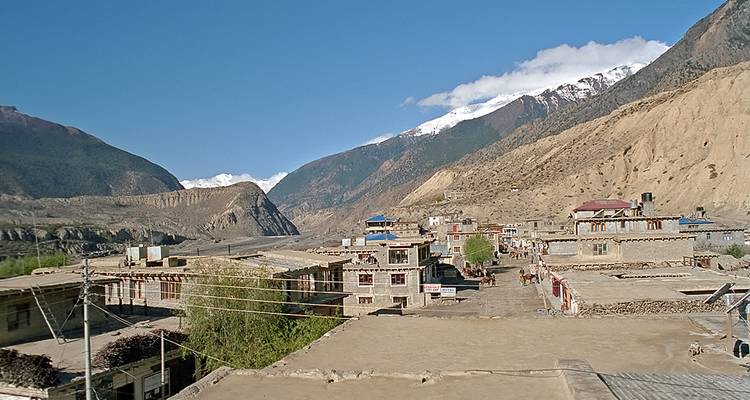 Village himalayen rural niché dans une vallée aride avec des sommets enneigés qui s'élèvent derrière.