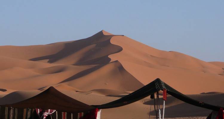 Rolling orange dunes of the Sahara with nomad tents in foreground against clear blue sky