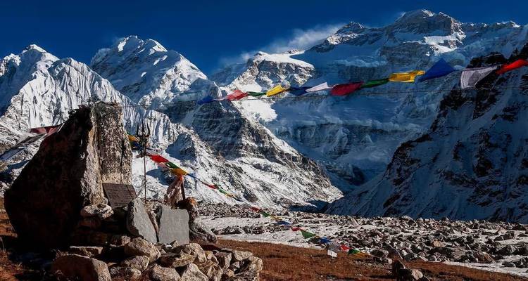 Sneeuw bedekte Himalaya pieken torenen boven gebedsvlaggetjes die fladderen naast een stenen herinnerings cairn.