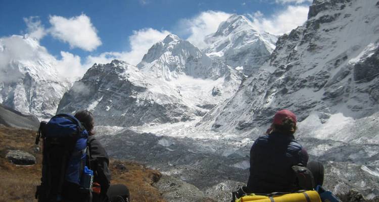 Rugzaktoeristen zitten op hun rugzakken en bewonderen de spectaculaire sneeuwbedekte bergkammen van de Himalaya onder een blauwe hemel.