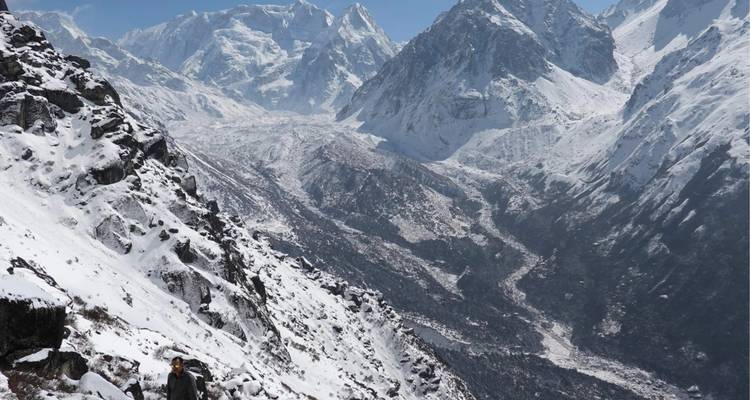 Uitgestrekte sneeuwwitte vallei omringd door ruige Himalayapieken met een eenzame trekker op het bergpad.