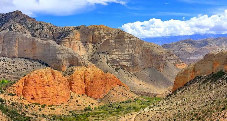 Kleurgestreepte rotswanden en een kronkelende groene vallei onder verspreide wolken in Upper Mustang.