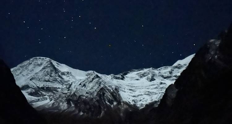 Nachtelijke scène van een sterrenhemel boven met gletsjers bedekte bergkammen omlijst door donkere valleien.