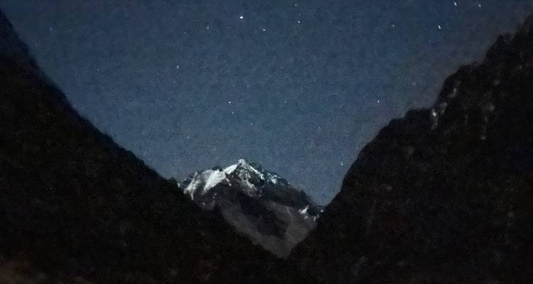 Vaag zichtbare bergtop tegen een korrelige nachtelijke hemel bezaaid met sterren.