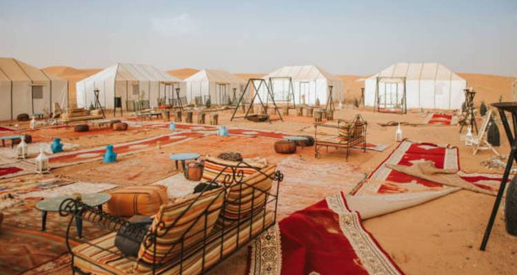 Wüstencamp mit weißen Zelten, Teppichen und Lounge-Bereichen auf orangefarbenem Sand