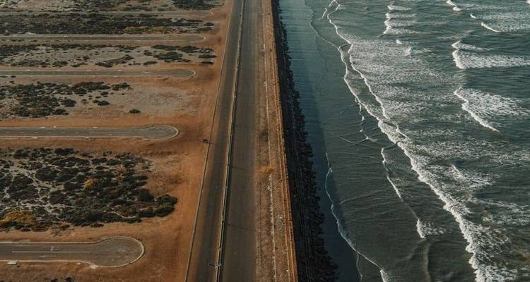 Aerial view of a coastal highway flanked by arid terrain on one side and ocean waves on the other
