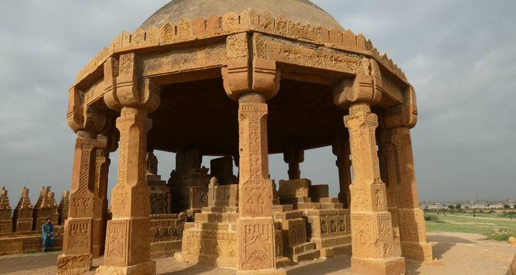Close view of a domed sandstone mausoleum with intricate carvings under a cloudy sky
