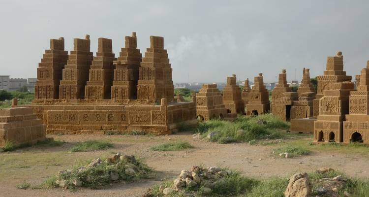Rows of sandstone funerary monuments standing on scrubby ground with city outskirts in distance