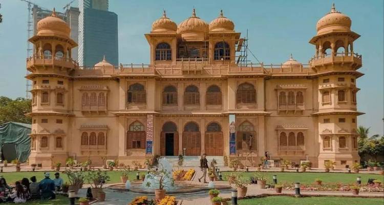 Sandstone palace-style museum building with domes and landscaped lawn in front
