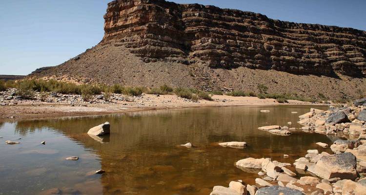 Shallow river reflecting layered basalt cliffs in a remote desert canyon.