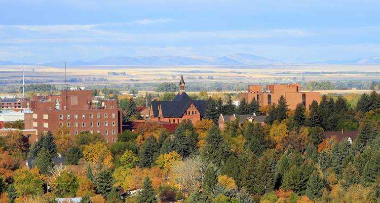 Vue d'automne sur un campus arboré avec des bâtiments en brique adossés à des plaines lointaines et des montagnes.