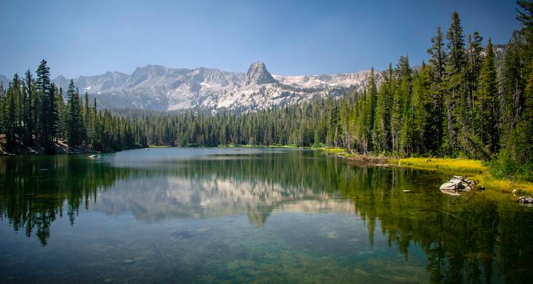 Lac cristallin reflétant les forêts de pins et les pics déchiquetés saupoudrés de neige sous un ciel dégagé.
