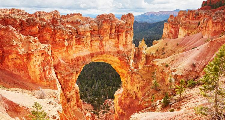 Natural arch of fiery orange hoodoos overlooking a forested canyon in Bryce Canyon National Park.