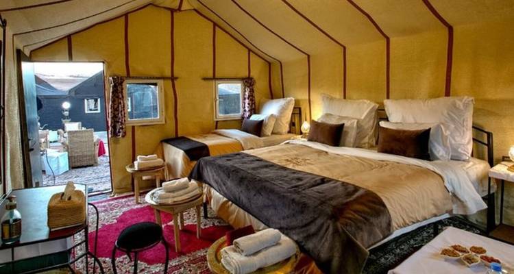 Innenraum eines luxuriösen Wüstenzelts mit weichen Betten, Teppichen und ordentlich arrangierten Handtüchern.