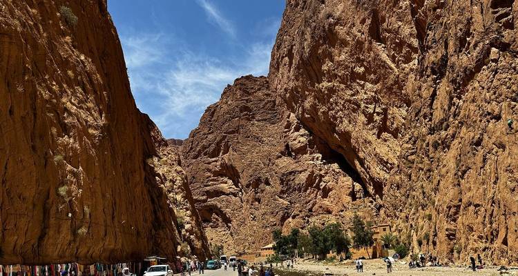 Sich auftürmende rote Felswände bilden den schmalen Korridor der Todra-Schlucht mit winzigen Menschen und Autos darunter.