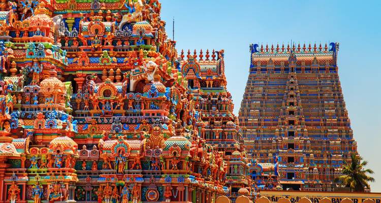 Des gopurams de temple dravidien aux couleurs vives couverts de divinités ornementées se dressent sous un ciel bleu dégagé.