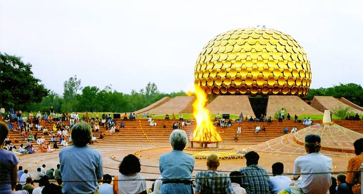 Des foules s'assoient sur des terrasses concentriques autour d'un feu de joie rituel avec le dôme doré étincelant du Matrimandir qui se dresse derrière.