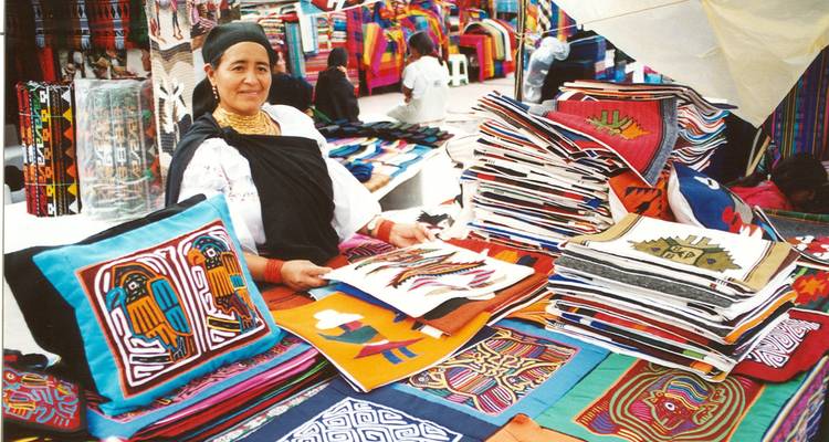 Indigener Verkäufer zeigt bunte gewebte Textilien auf dem Markt von Otavalo