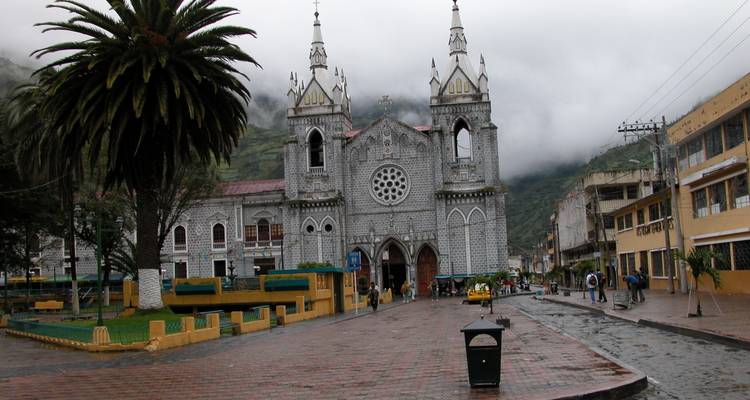 Gotische Basilika aus grauem Stein in der regnerischen Bergstadt Baños mit nebligen Hügeln im Hintergrund