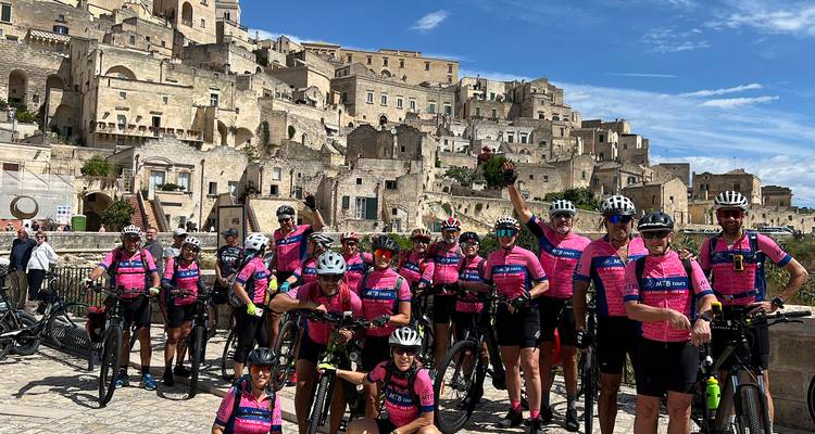 Grand groupe de cyclistes en maillots roses vifs se rassemblent avec leurs vélos devant le paysage urbain de pierre de Matera.